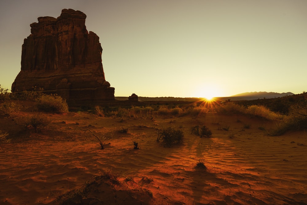 the sun is setting behind a rock formation in the desert