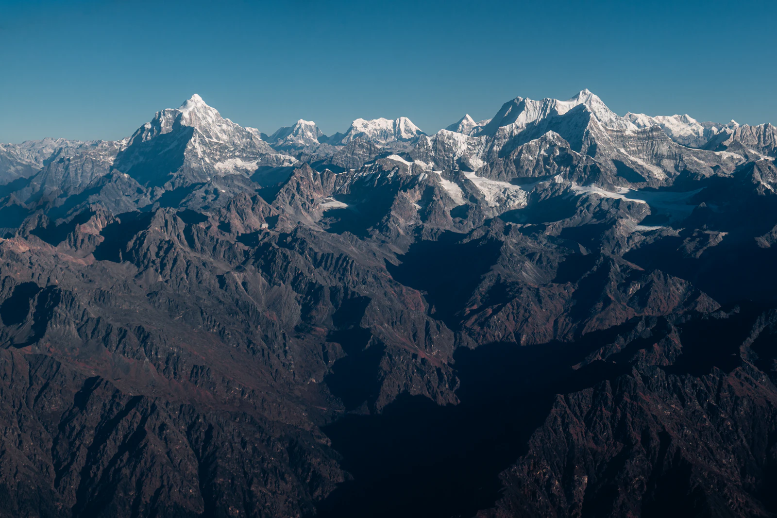 Gauri Shankar and Melungtse standing above dark folded ridges, seen from the window of a mountain flight out of Kathmandu