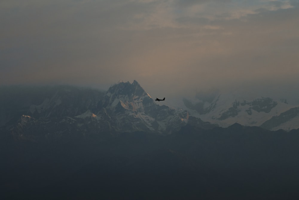 a plane flying over a mountain range under a cloudy sky