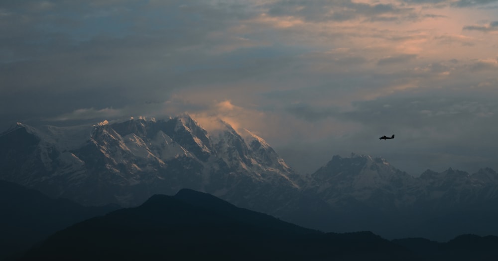 a plane flying over a mountain range under a cloudy sky