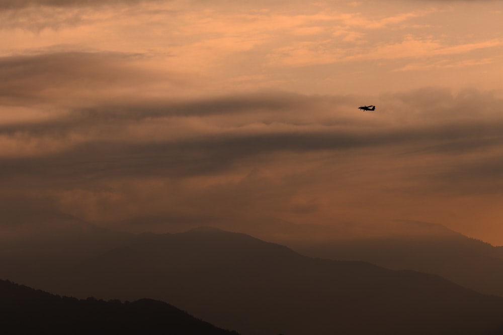 un avión volando a través de un cielo nublado con montañas en el fondo