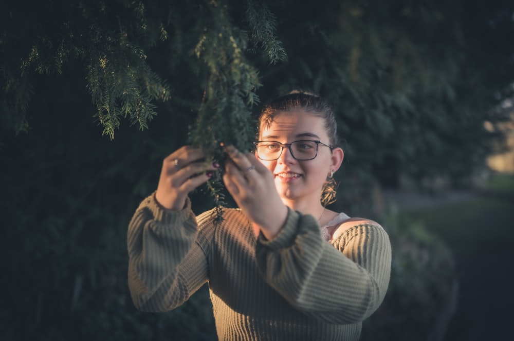 a woman wearing glasses holding a branch of a tree