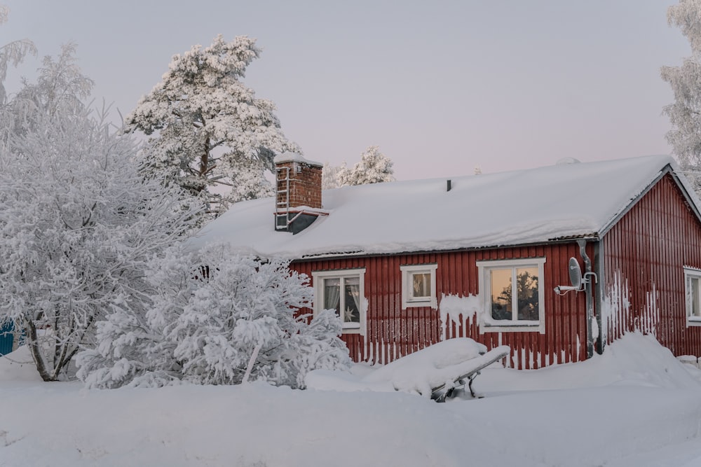 a red house covered in snow next to trees