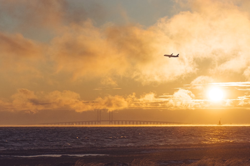 a plane flying over a body of water at sunset