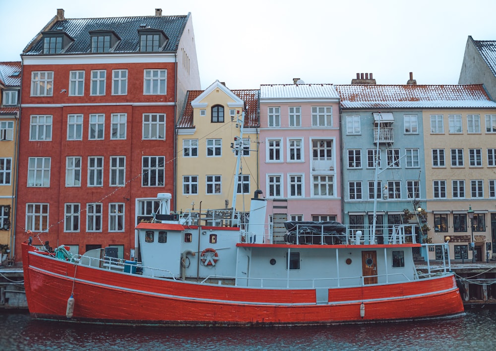 a red and white boat in front of a row of buildings