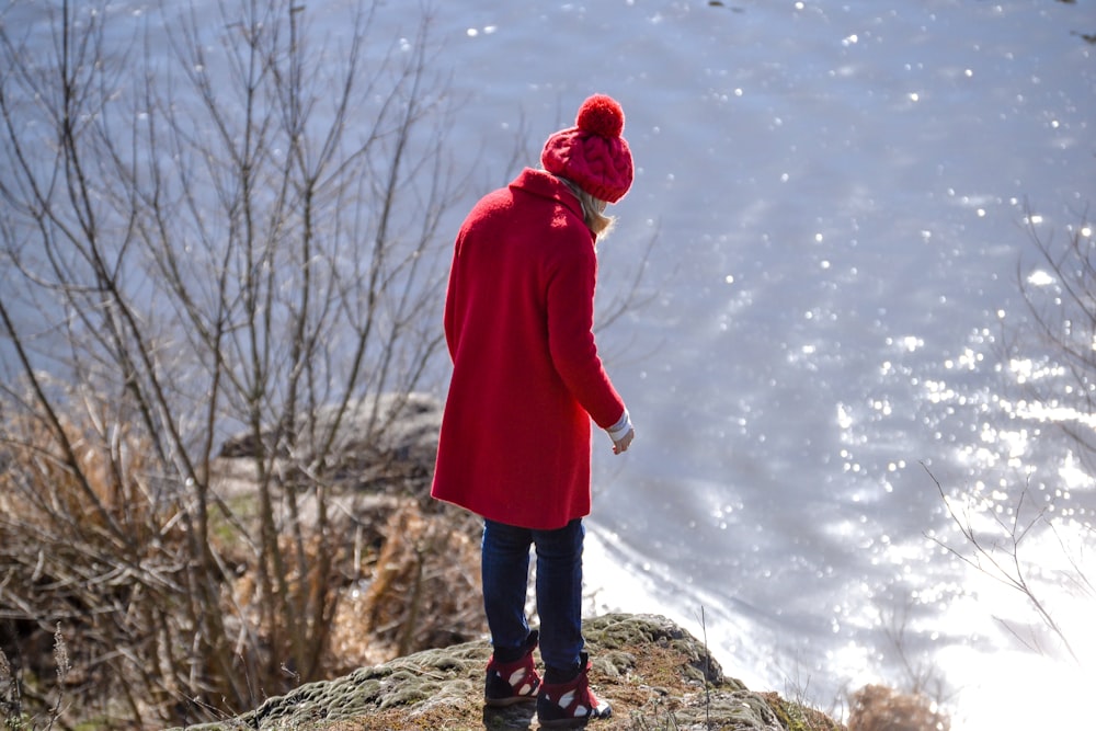 a woman in a red coat is standing on a rock