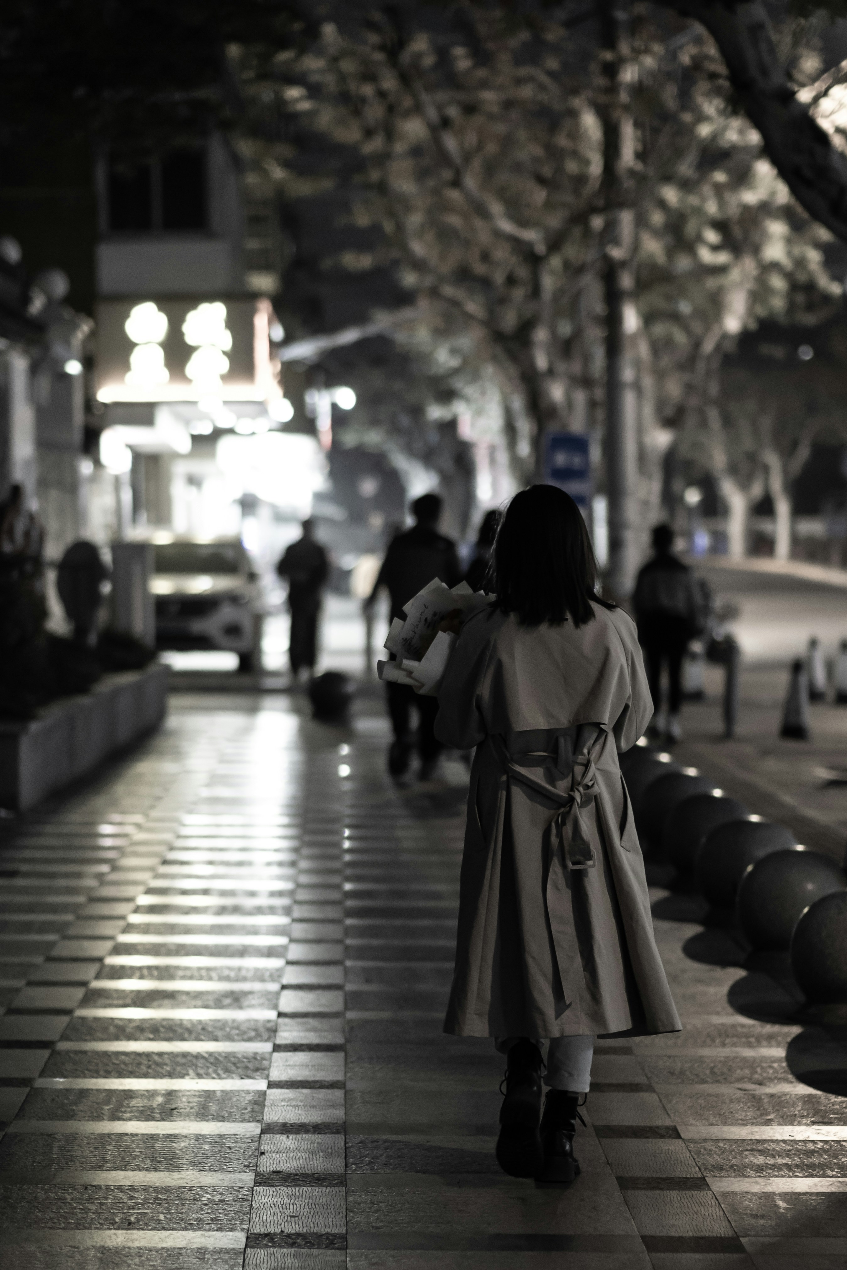 a woman walking down a sidewalk at night