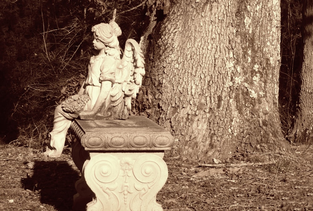 a statue of an angel sitting next to a tree