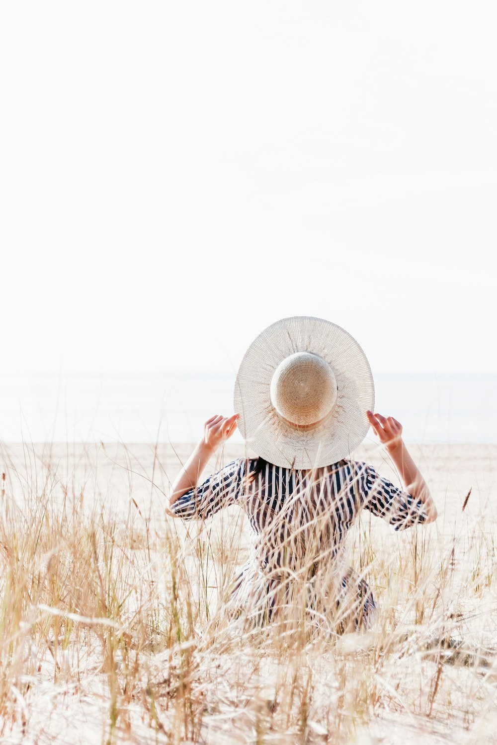 Una donna con un cappello è seduta sulla sabbia
