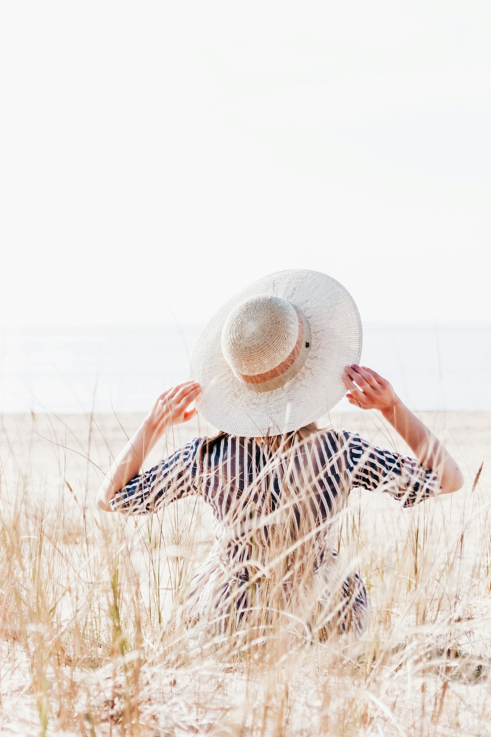 a woman in a striped dress and hat in the sand