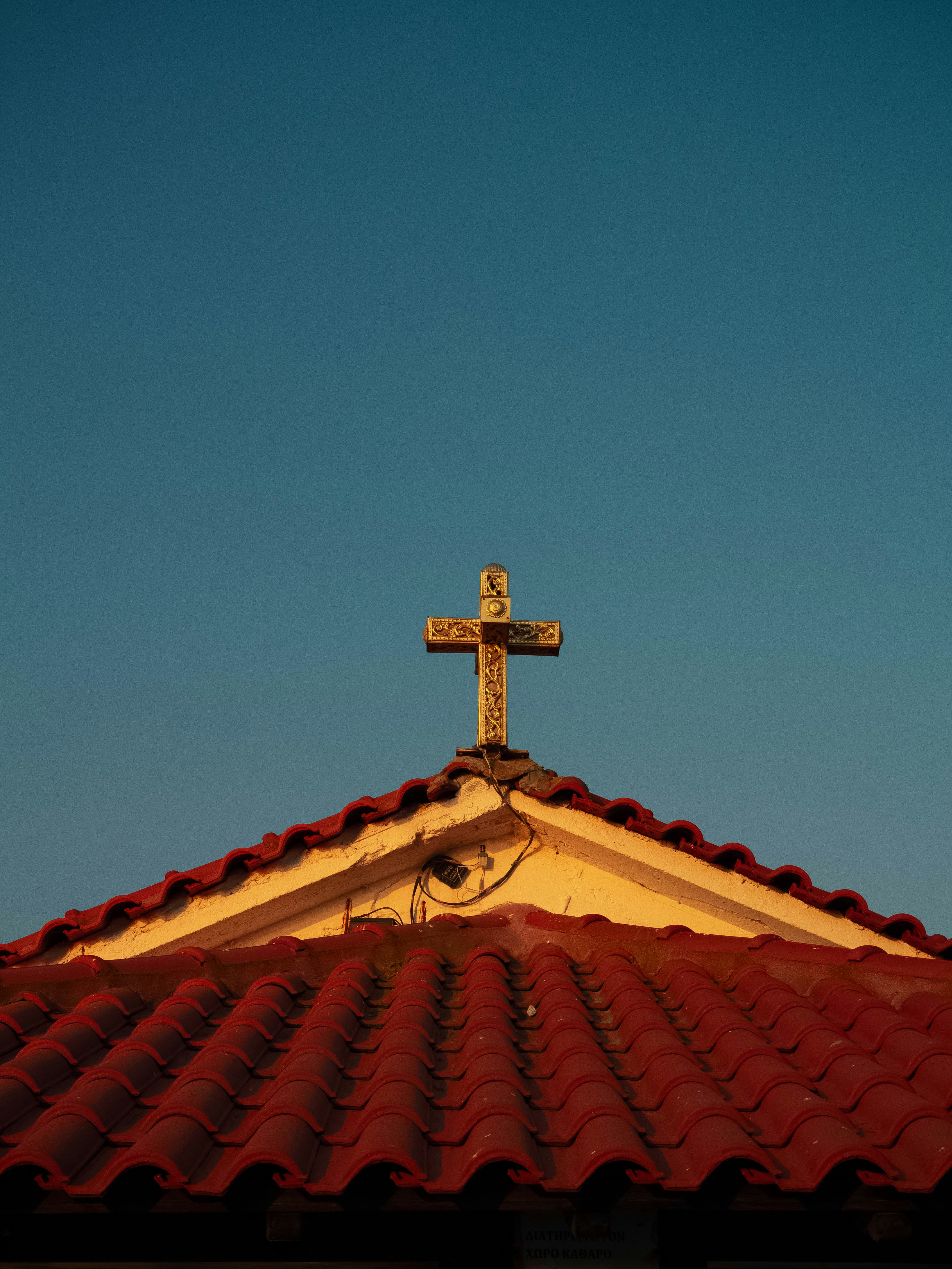 a cross on top of a roof with a blue sky in the background