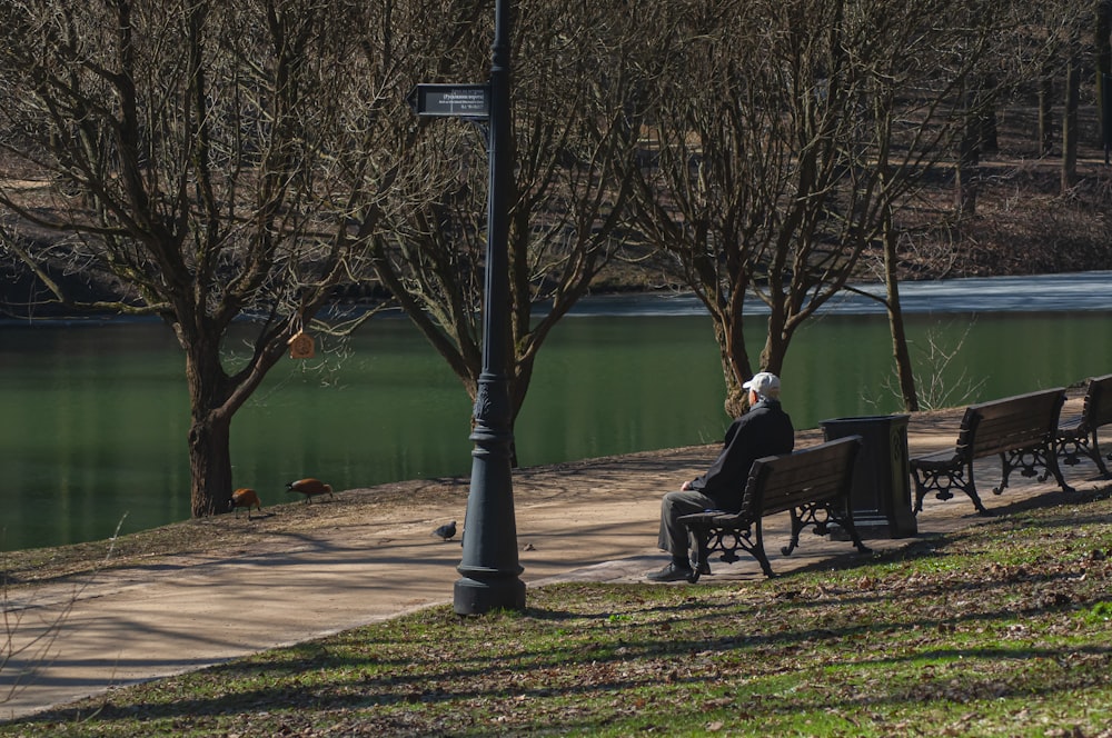 a man sitting on a park bench next to a lake