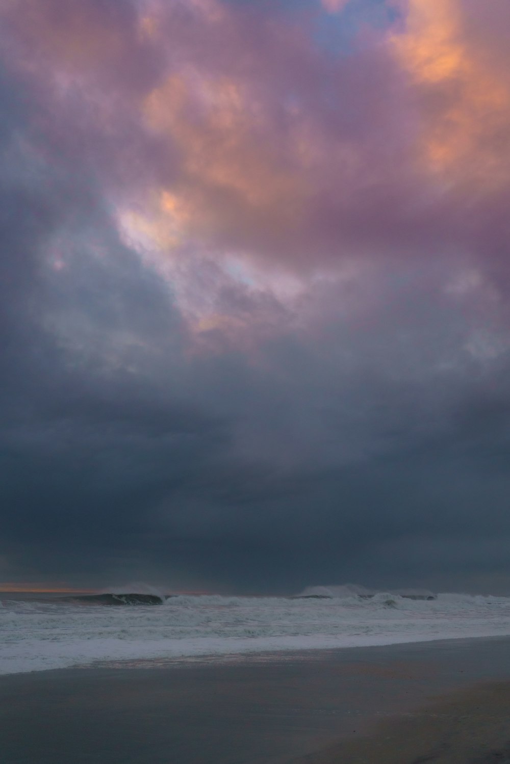 a person walking on a beach with a surfboard under a cloudy sky