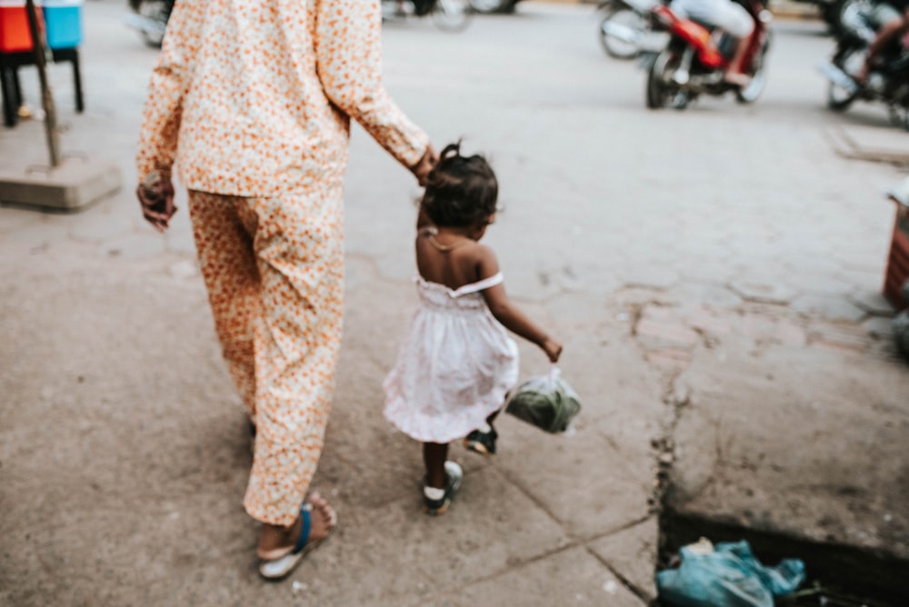 a woman holding the hand of a little girl