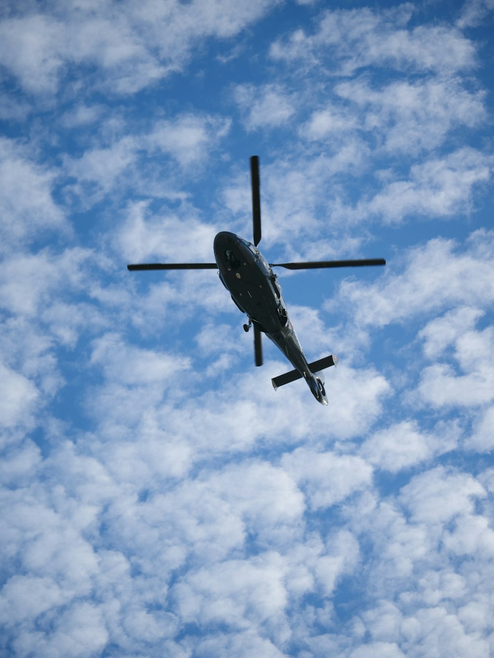 a helicopter flying through a cloudy blue sky