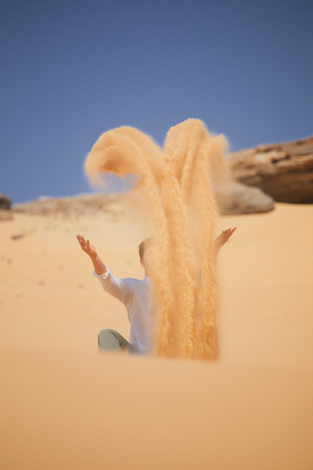 un uomo seduto sulla sabbia che lancia sabbia in aria