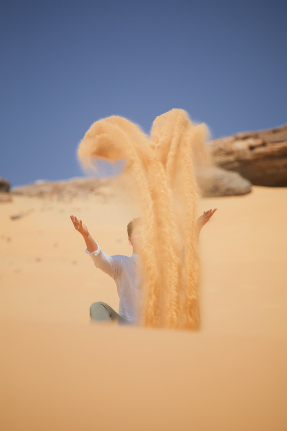 a man sitting in the sand throwing sand into the air