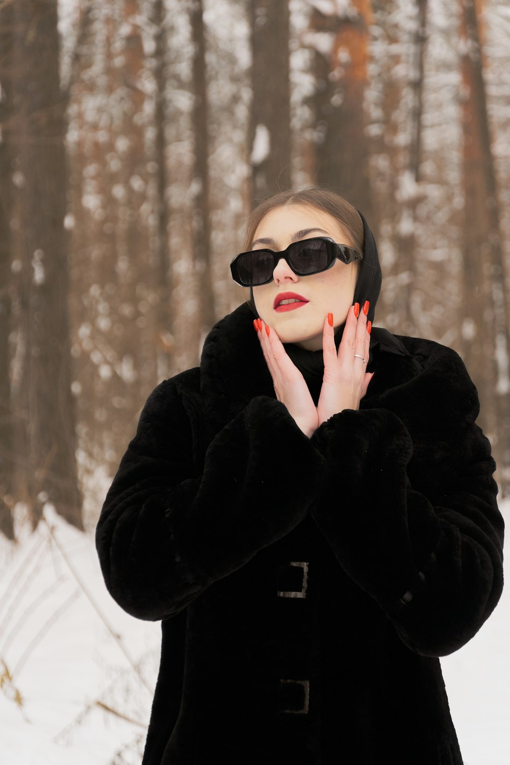 a woman in a black coat and sunglasses standing in the snow