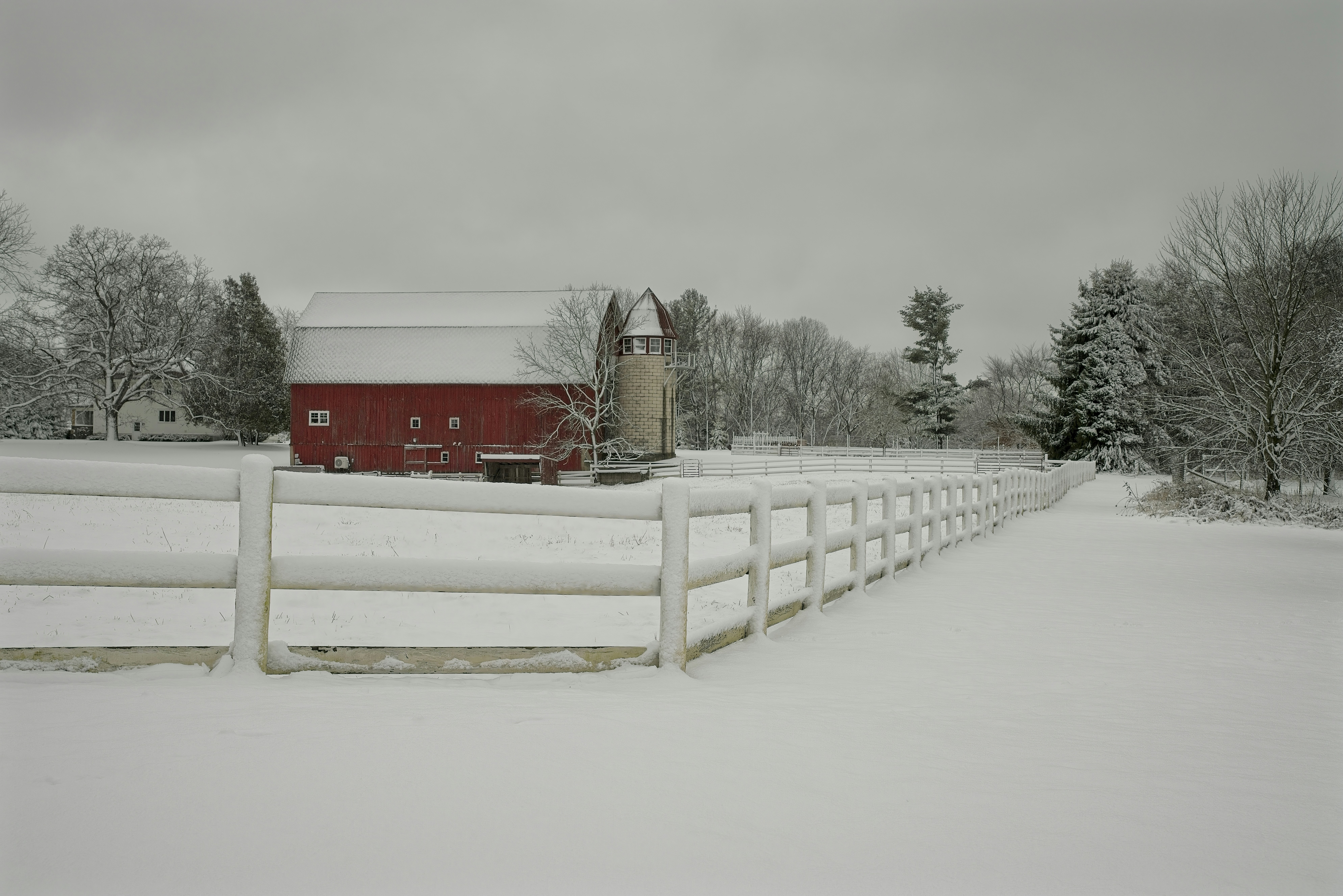 a red barn and a white fence in the snow