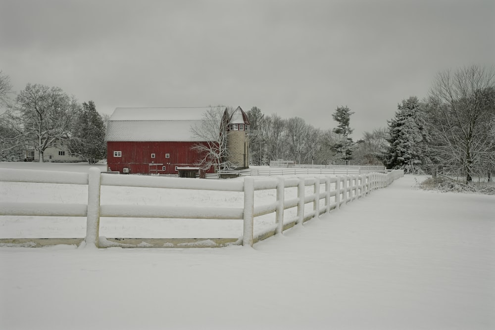 a red barn and a white fence in the snow