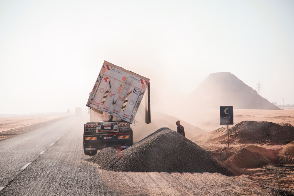 a truck driving down a dirt road next to a pile of dirt