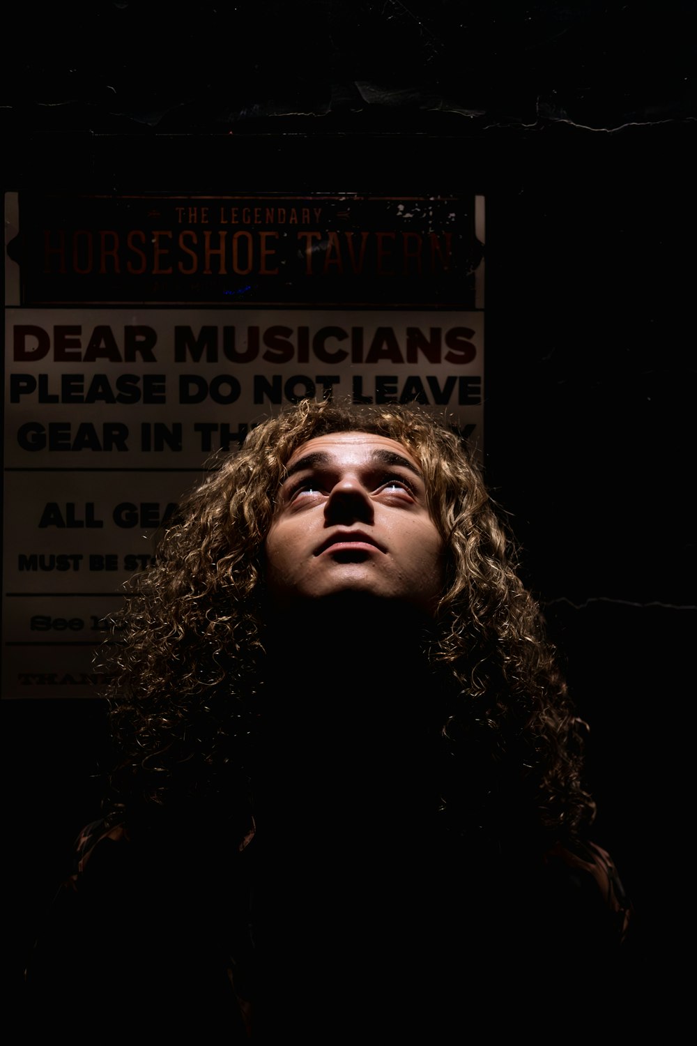 a man with long curly hair standing in front of a sign