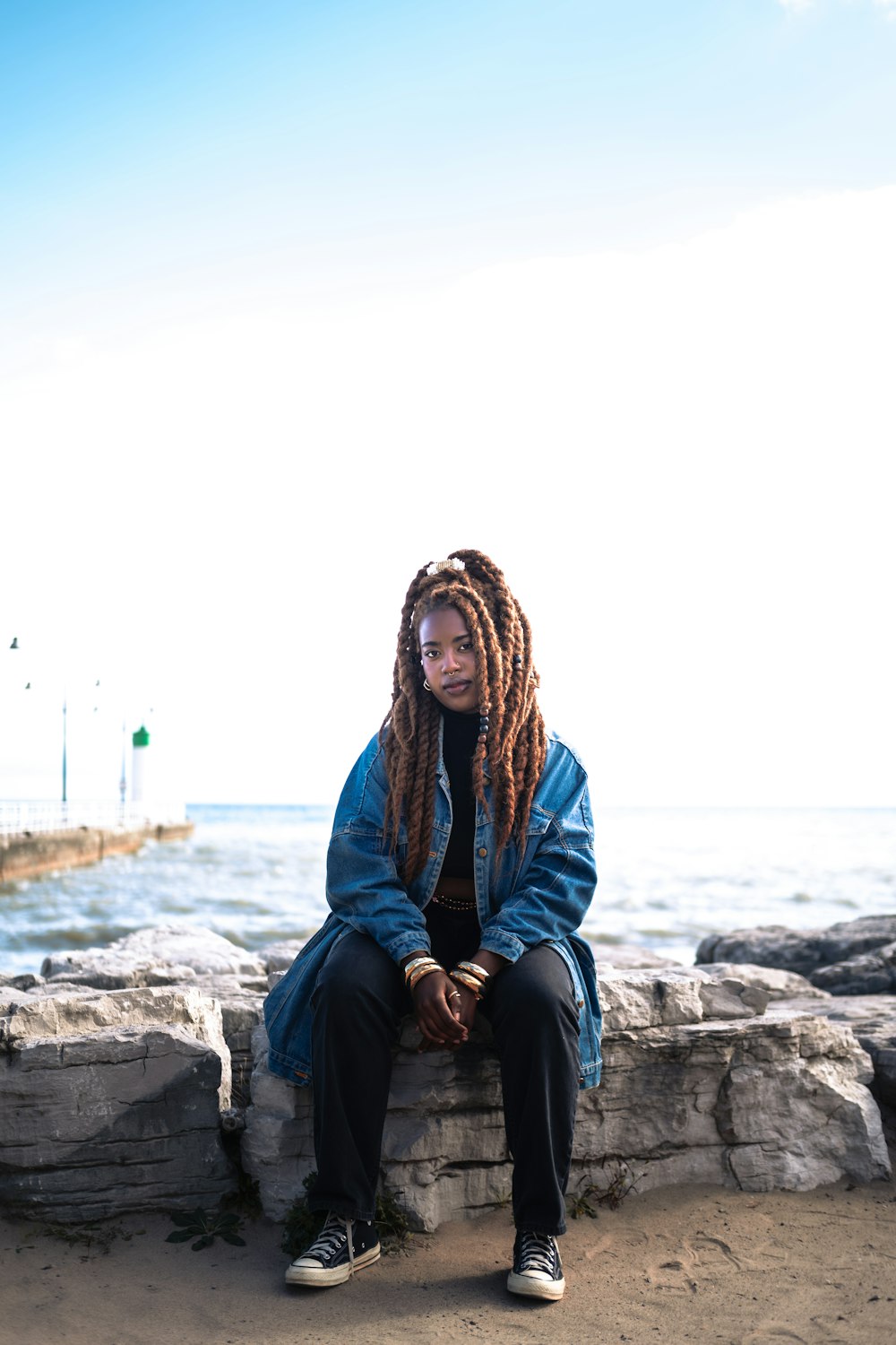 a woman with dreadlocks sitting on a rock near the ocean