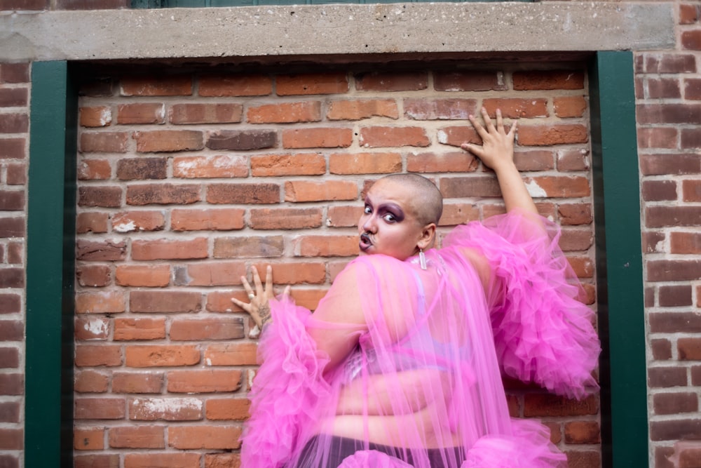 una mujer con un vestido rosa de pie frente a una pared de ladrillos