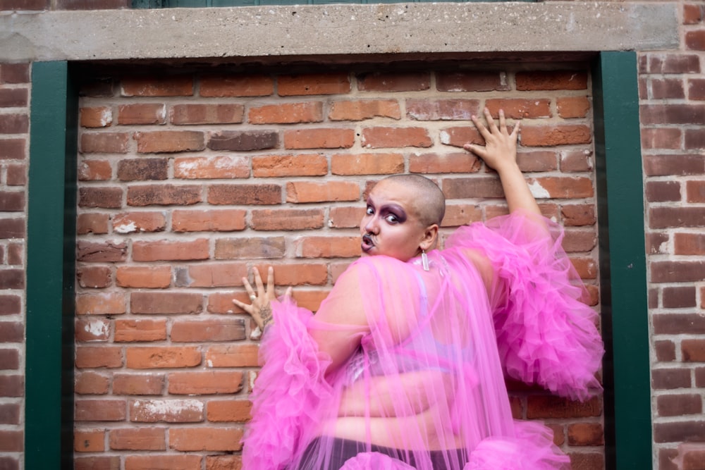 a woman in a pink dress standing in front of a brick wall