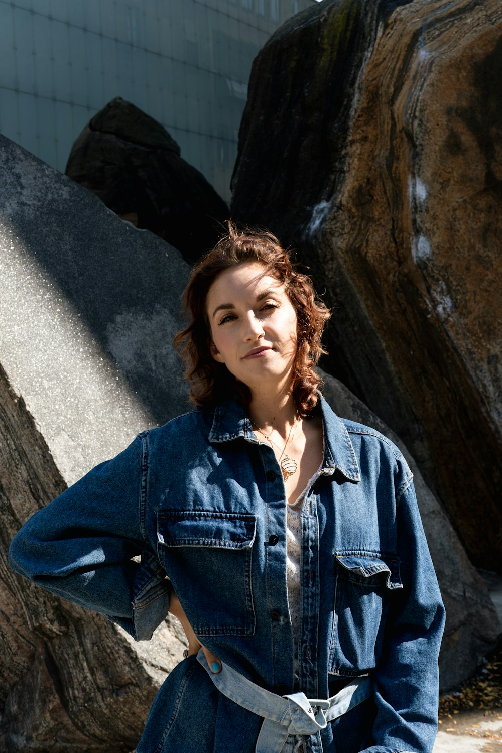 a woman wearing a jean jumpsuit standing in front of a rock formation