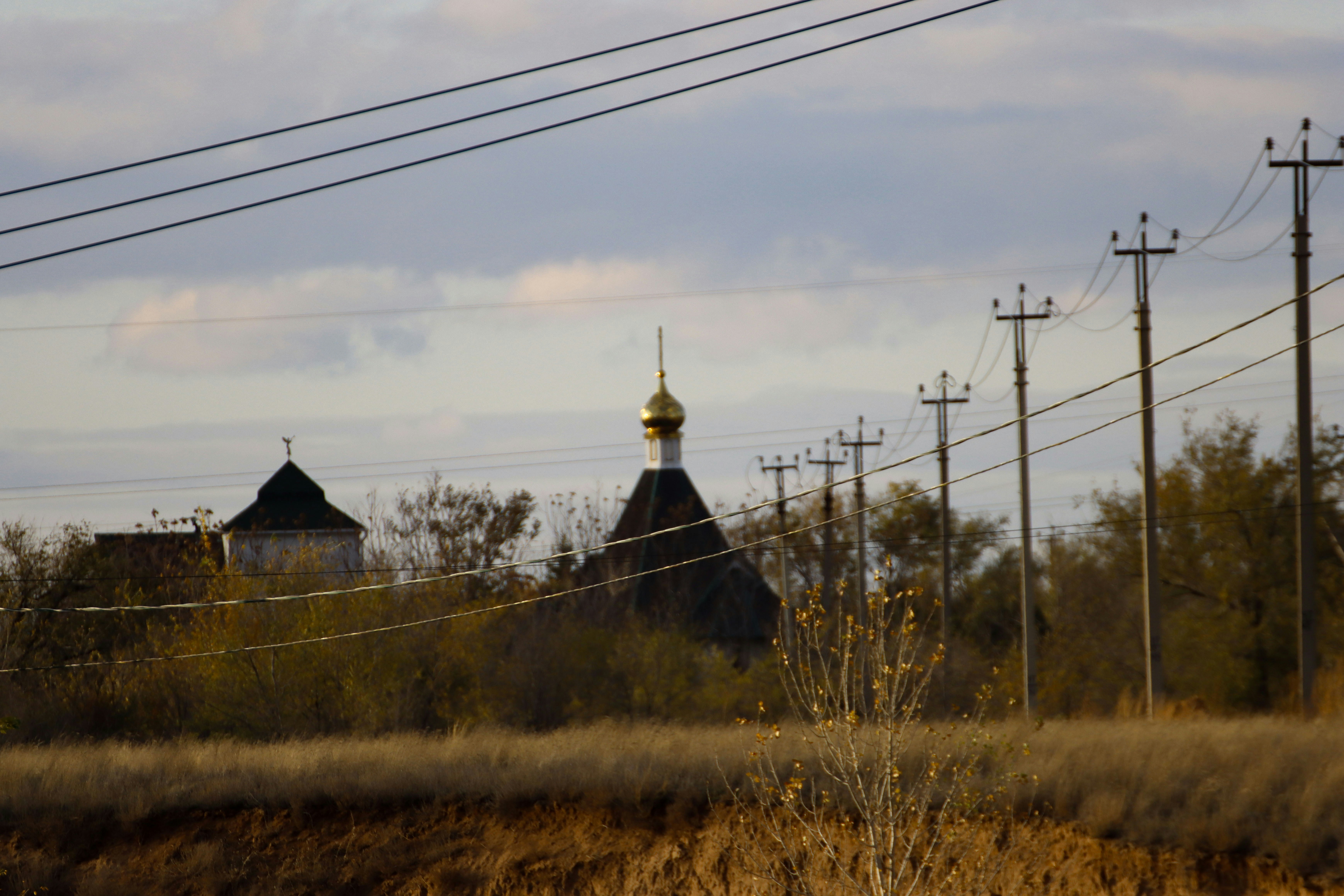 a grassy field with power lines and a church in the background