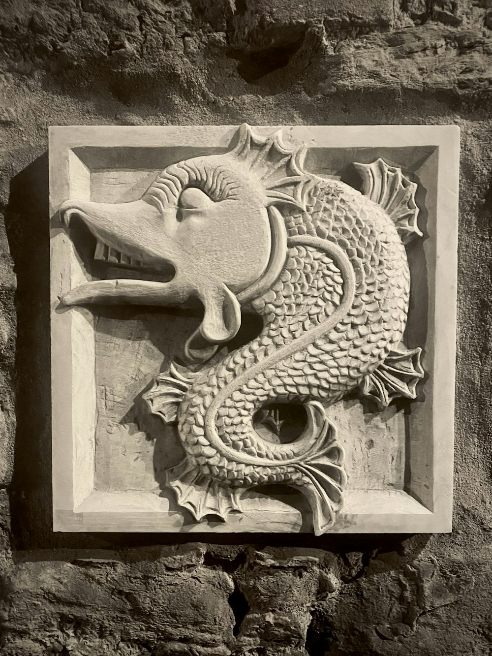 uma foto em preto e branco de um dragão em uma parede de pedra