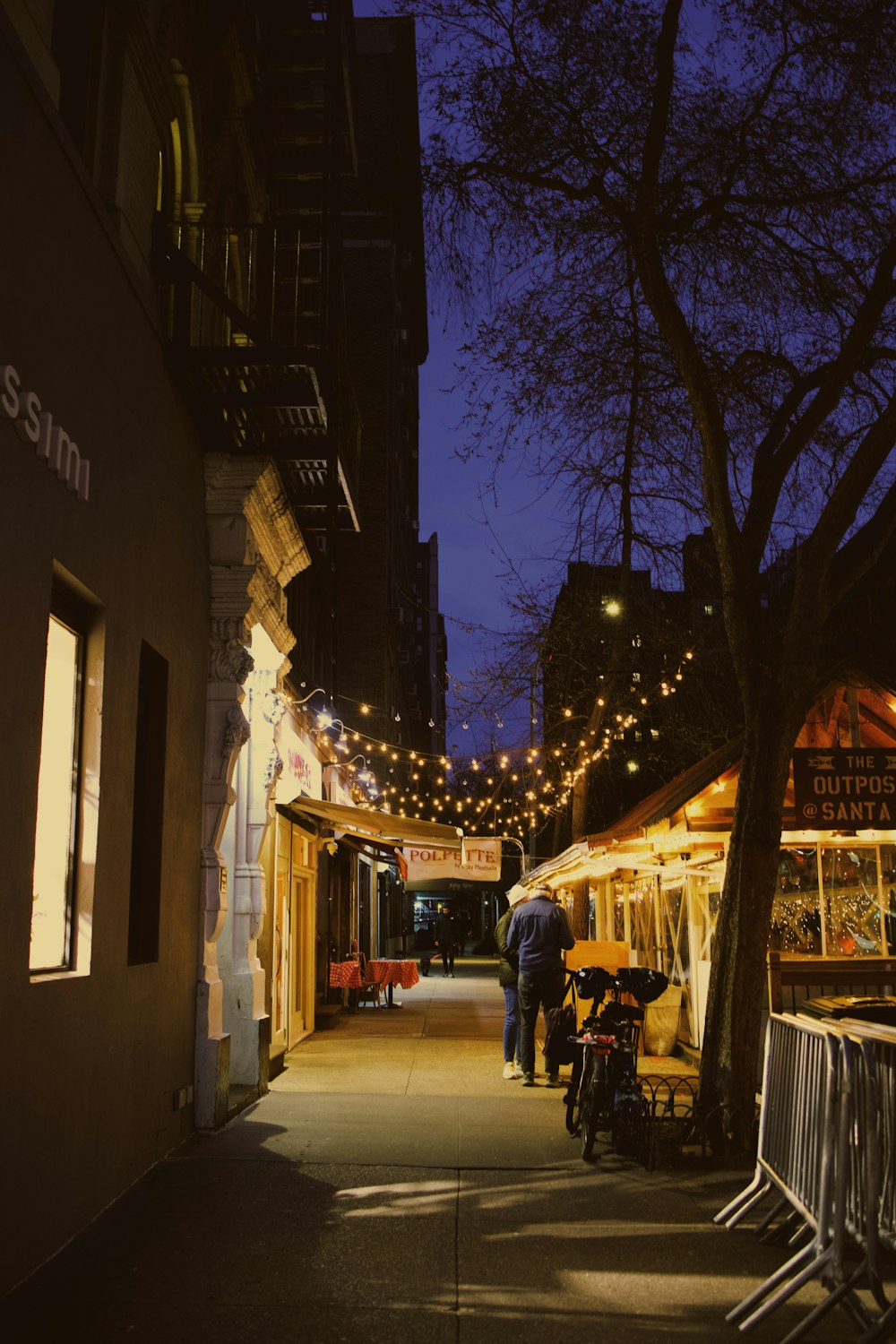 a couple of people walking down a street next to a tree