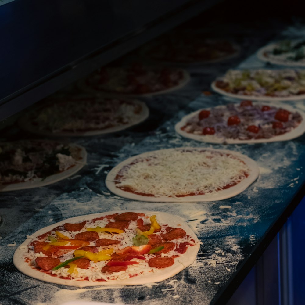 a row of uncooked pizzas sitting on top of a counter