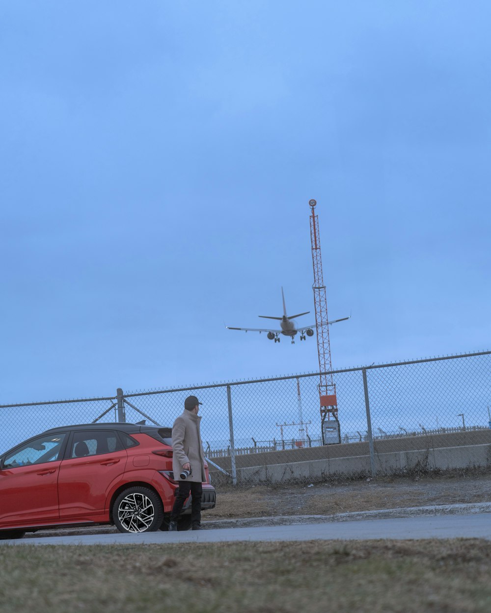 a man standing next to a red car in front of a fence