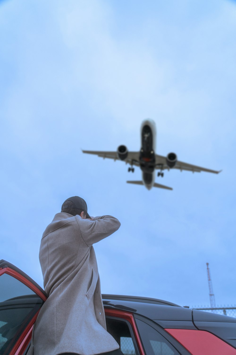 a man leaning on a car looking at an airplane