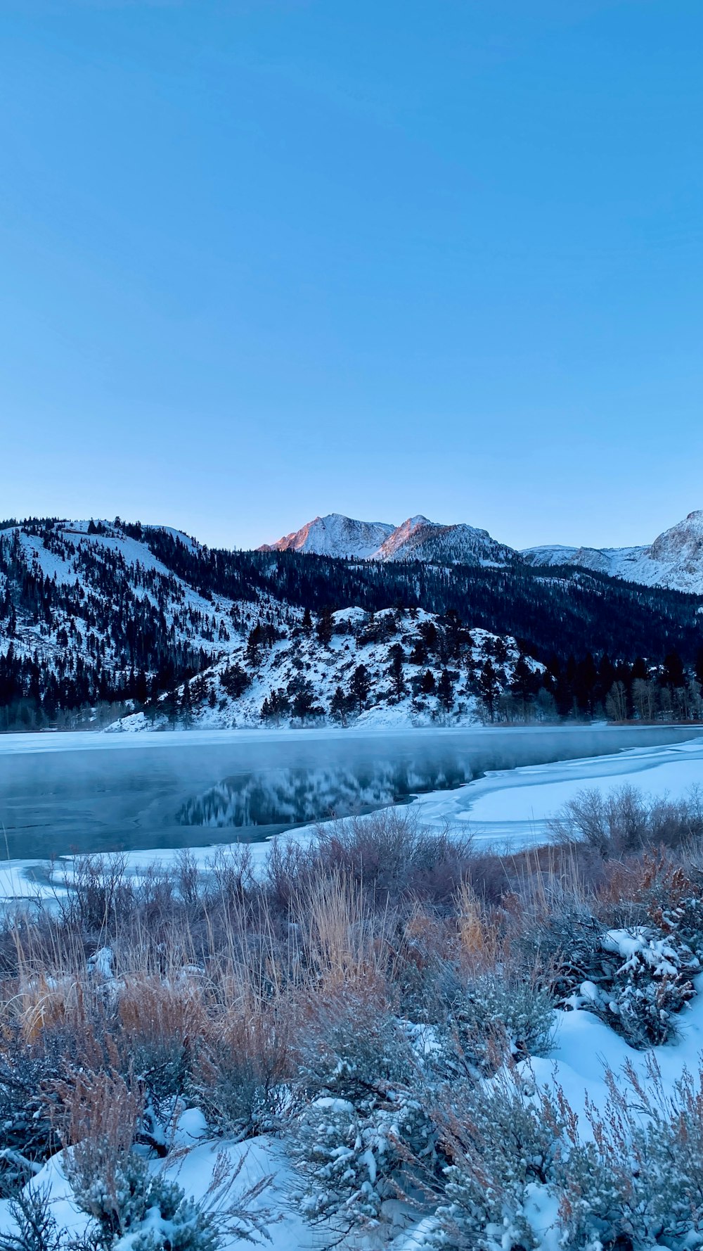 una vista panorámica de un lago de montaña con nieve en el suelo