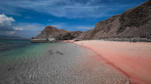 a beach with a pink sand and a mountain in the background