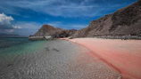 a beach with a pink sand and a mountain in the background