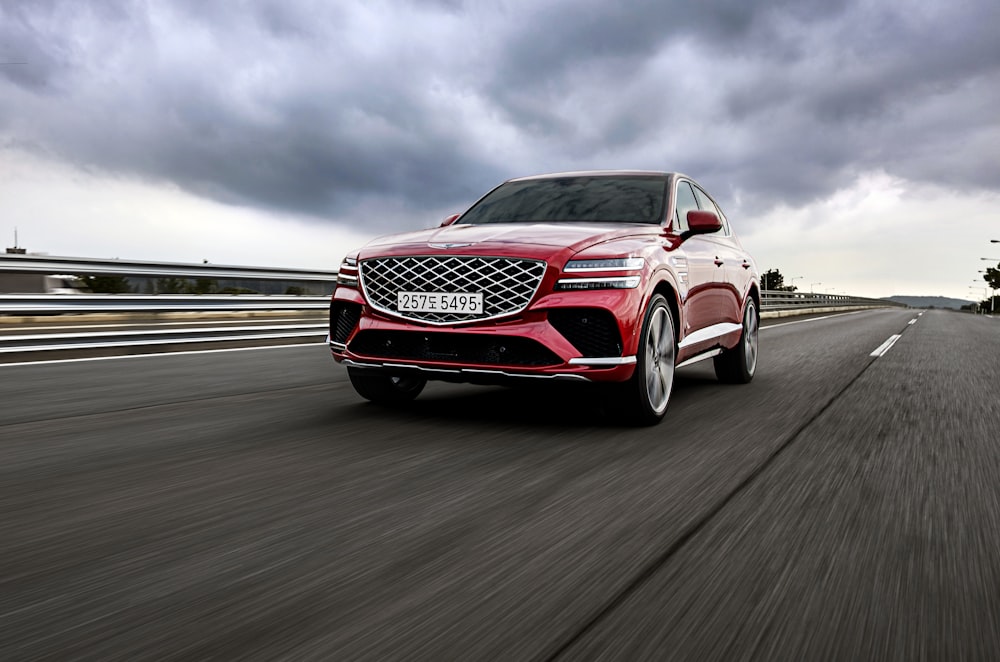 a red car driving down a road under a cloudy sky