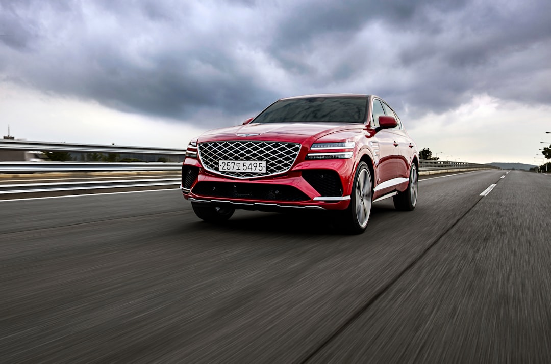 a red car driving down a road under a cloudy sky, The Genesis GV80 Coupe speeding through a road on a cloudy day.