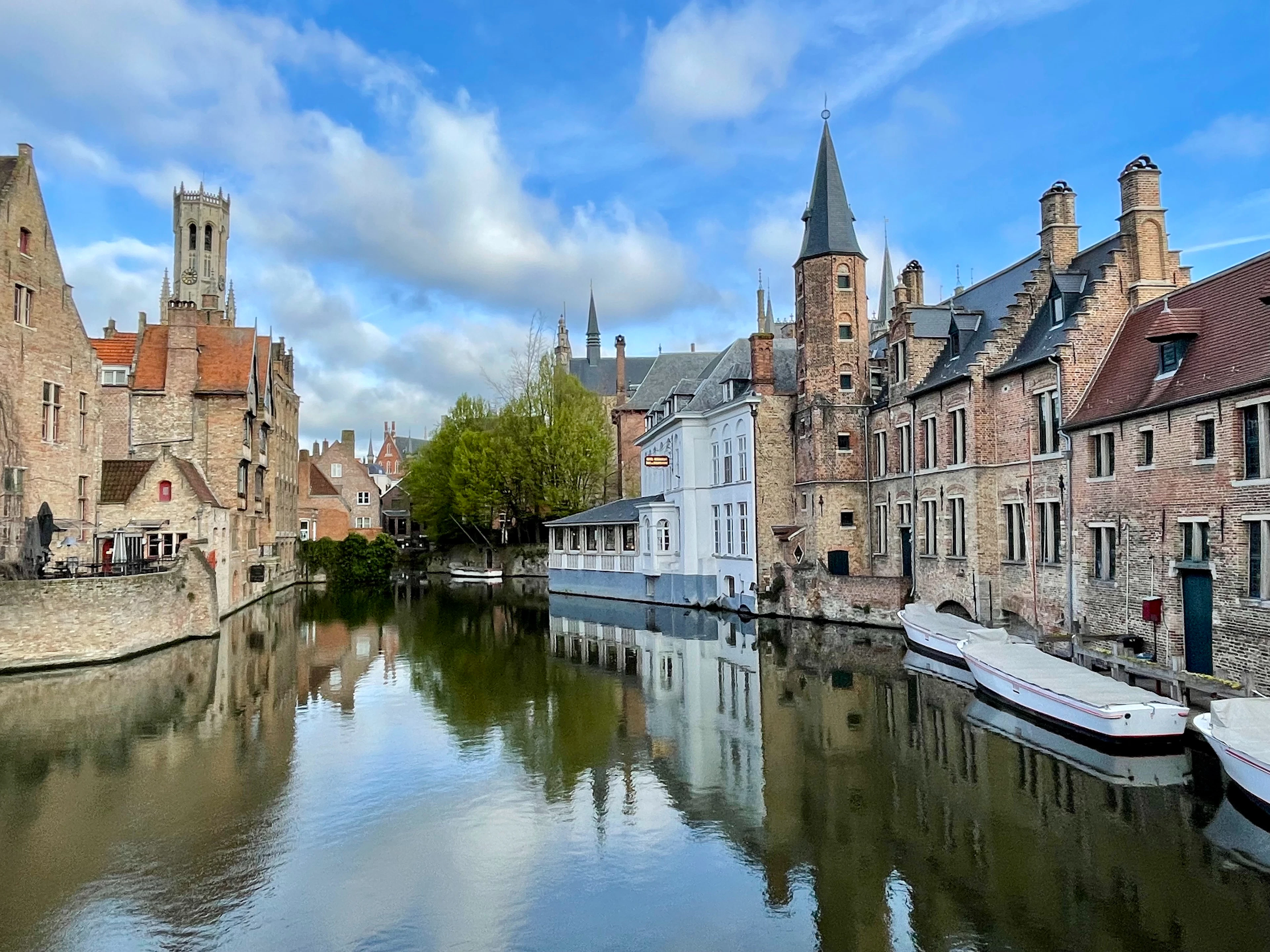 The Rozenhoedkaai canal corner in Bruges, its gabled houses and distant belfry mirrored in calm water.