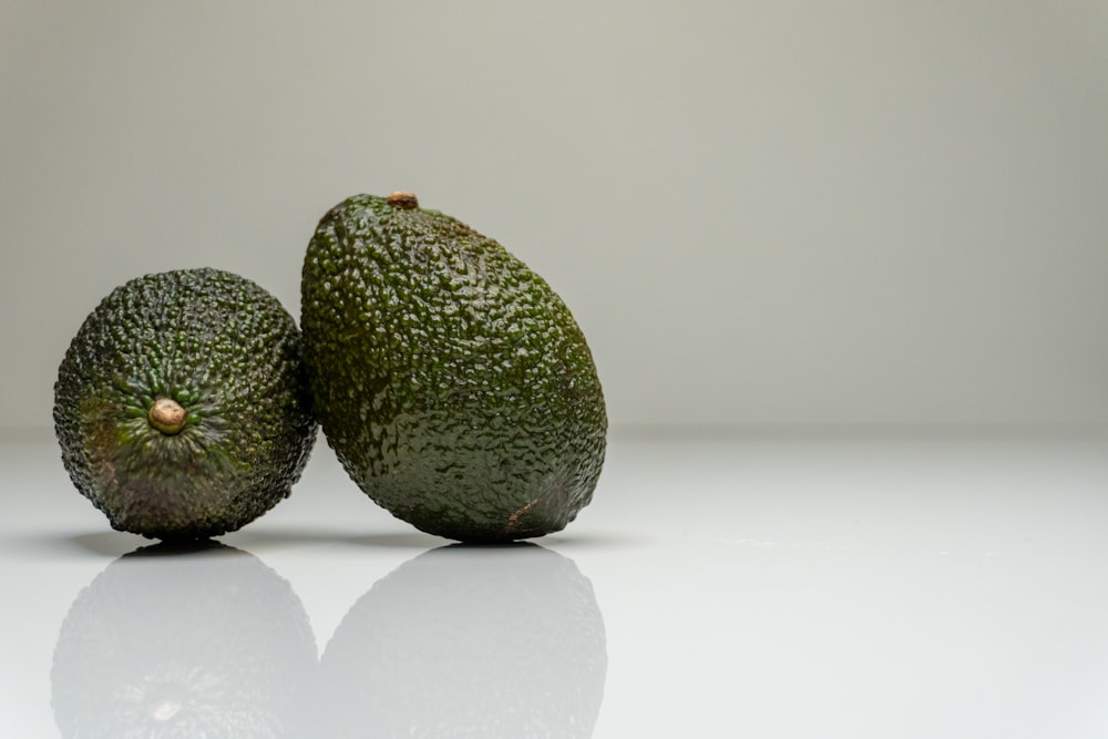 two avocados sitting side by side on a white surface