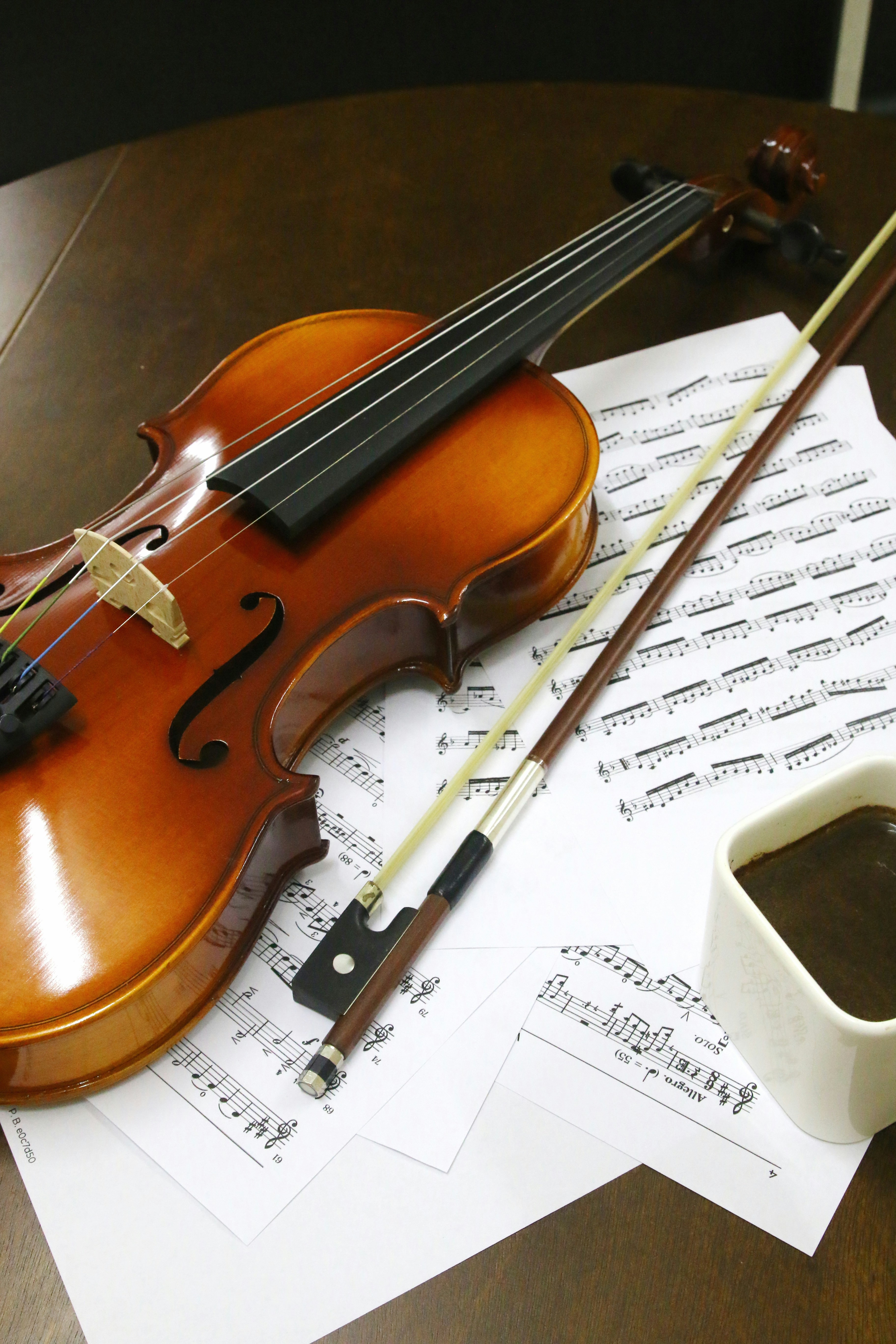 a violin sitting on top of sheet music next to a cup of coffee