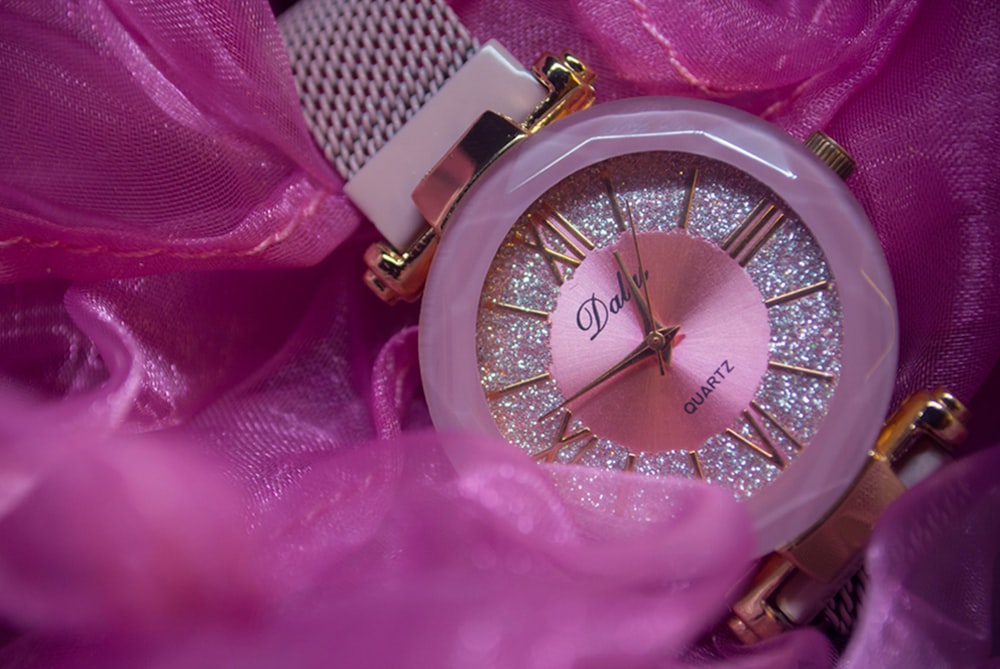 um close up de um relógio em um pano rosa