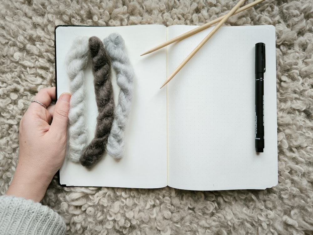 une main tient une aiguille à tricoter au-dessus d’un livre