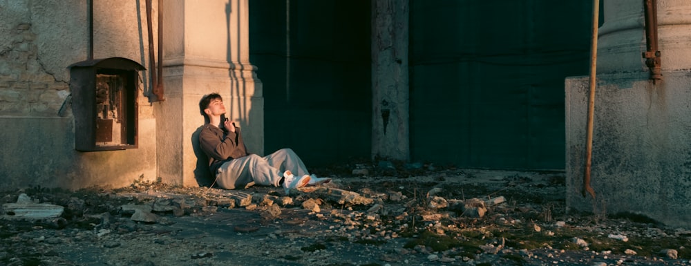 a man sitting on the side of a building talking on a cell phone