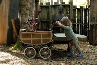 a little girl pushing a wagon with a statue of a man in the background