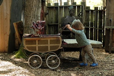 a little girl pushing a wagon with a statue of a man in the background