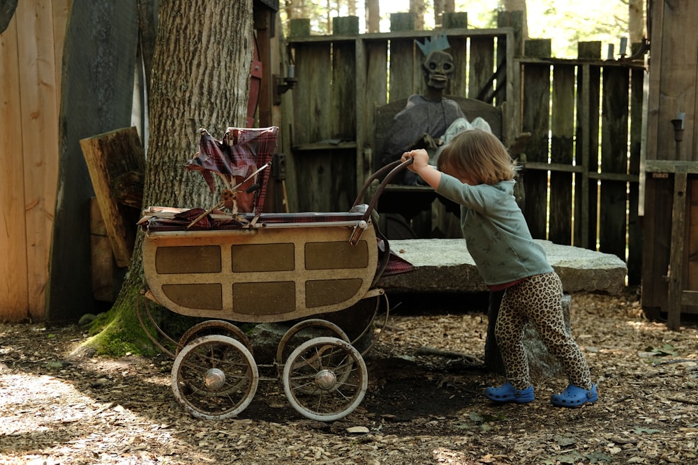 a little girl pushing a wagon with a statue of a man in the background